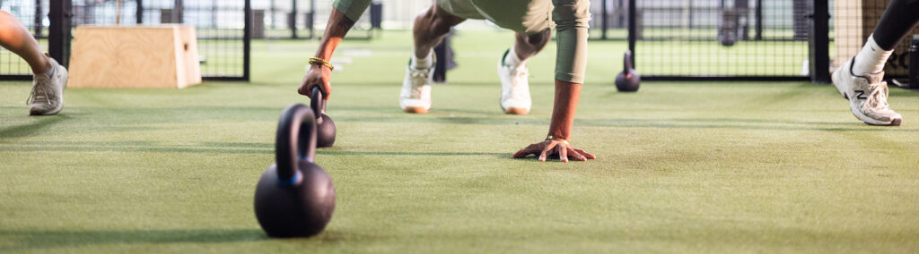 Group fitness class performing kettlebell push-up exercises on turf at Replay Club gym