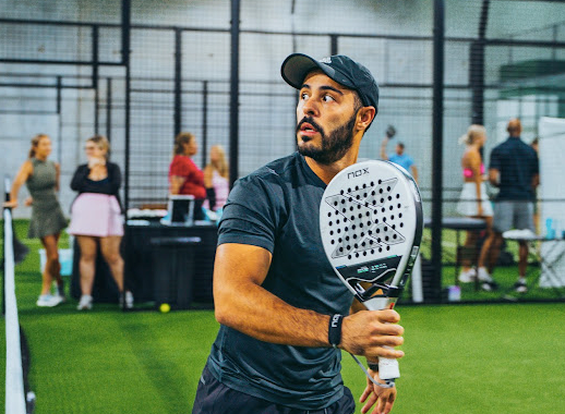 A person holding a padel racquet in the middle of a game at Replay Club. 